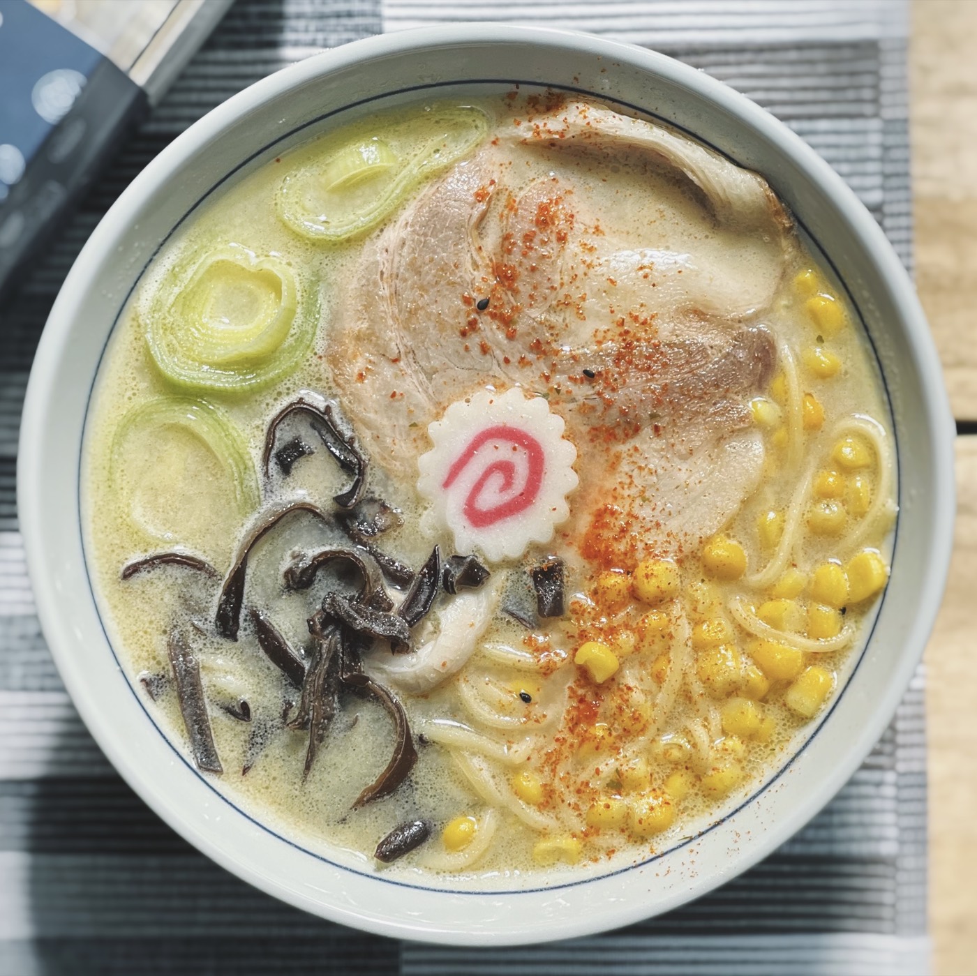 A bowl of creamy tonkotsu ramen with char siu, sweetcorn, leek and fish cake, seen from above