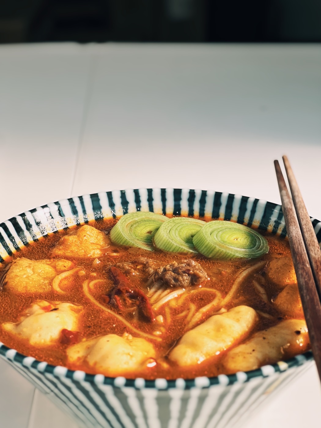 A close-up of spicy beef noodles with fish balls, tofu puffs and leek